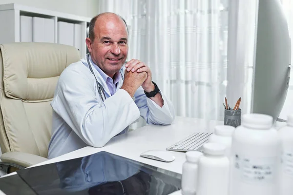 Πορτρέτο Χαμογελαστή Έμπειρη Γιατρός Ποδιά Κάθεται Στο Τραπέζι Του Γραφείου — Φωτογραφία Αρχείου