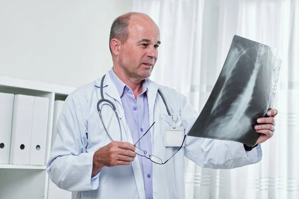 严重的白种放射科医生摘下眼镜 看着肺部X光片在他的手中 — 图库照片