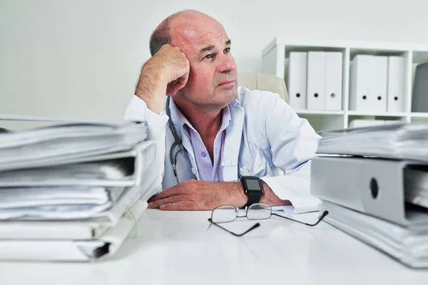 Volwassen Huisarts Zittend Aan Zijn Tafel Geplunderd Met Bindmiddelen Documenten — Stockfoto