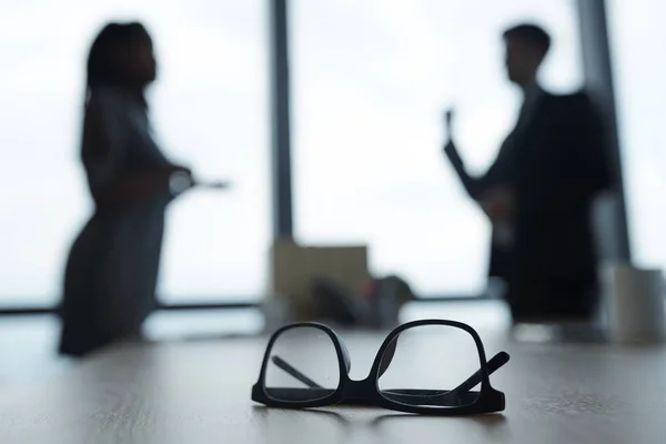 Gafas Mesa Oficina Siluetas Ejecutivos Negocios Discutiendo Noticias Segundo Plano — Foto de Stock