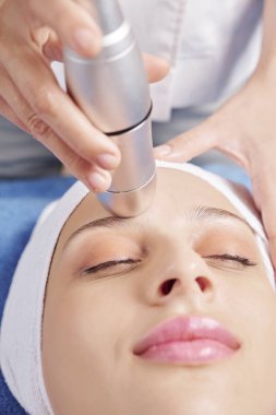 Kadın müşteriye profesyonel cilt bakımı verirken özel makine kullanan kozmetolojist
