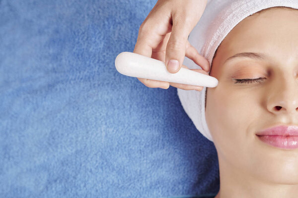 Close-up image of beautician using quartz stick to massage area around eyes and get rid of under eye wrinkles
