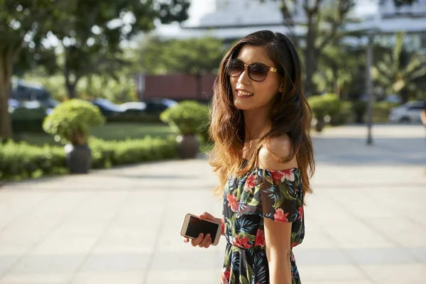 在阳光明媚的夏日户外散步时 戴着太阳镜的快乐美丽的年轻女子手持智能手机的肖像 — 图库照片