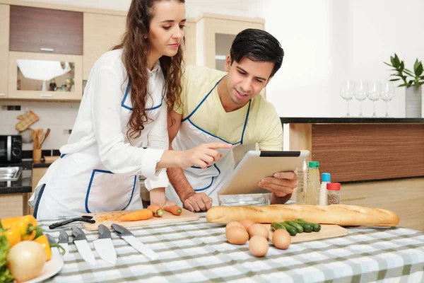 Giovane Coppia Caucasica Grembiuli Ricetta Lettura Tablet Computer Prima Cucinare — Foto Stock