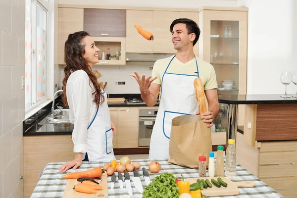 微笑英俊的年轻人在妻子面前从购物袋里拿出蔬菜时 会大笑着 一边大手大脚 — 图库照片