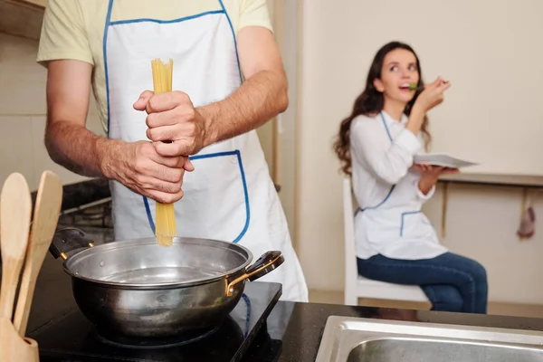年轻人把意大利面在沸水中时 他的妻子吃沙拉的背景 — 图库照片