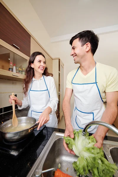 漂亮的微笑年轻女子和她的丈夫煮意大利面和洗生菜的美味菜 — 图库照片