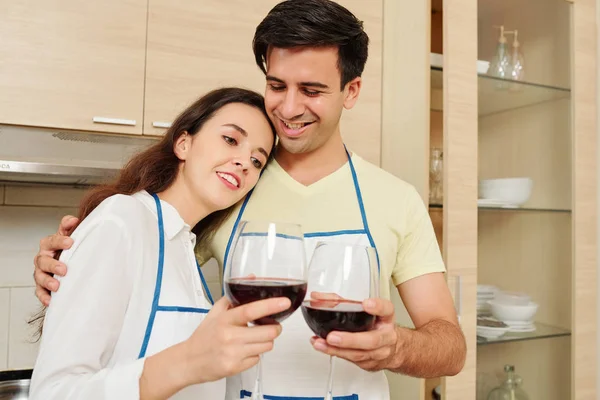 エプロンでポジティブな若い白人のカップルは キッチンに立って 一緒に調理した後 赤ワインを飲みます — ストック写真