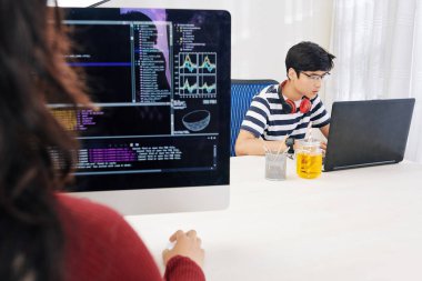 Ofiste dizüstü bilgisayarda Konsantre Asyalı genç programlama, onun kadın arkadaşı bilgisayarda yeni yazılım oluşturma
