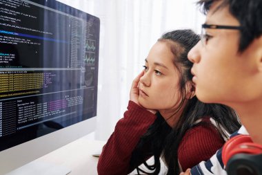 Yorgun genç kız sınıf arkadaşının bilgisayar ekranında programlama kodu bakarak