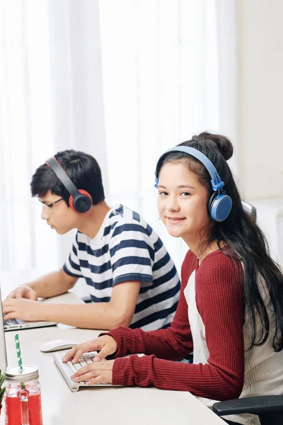 微笑漂亮的亚洲少女听耳机音乐 并在她在课堂上的桌子上工作 — 图库照片