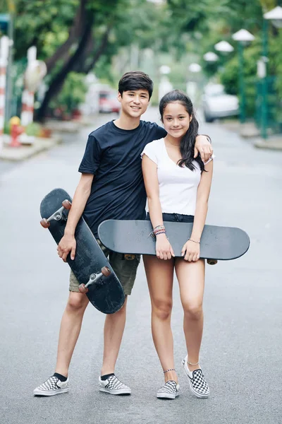 拥抱十几岁的兄弟姐妹站在街上与滑板在手 — 图库照片