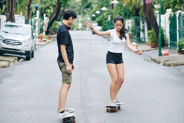 夏の日に道路に沿ってスケートボードに乗るために姉妹を教える十代の少年 — ストック写真