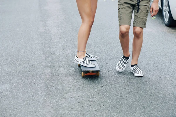 スケートボードに乗って 彼女が落ちないように助ける彼のガールフレンドの隣を歩く男の子の足 — ストック写真
