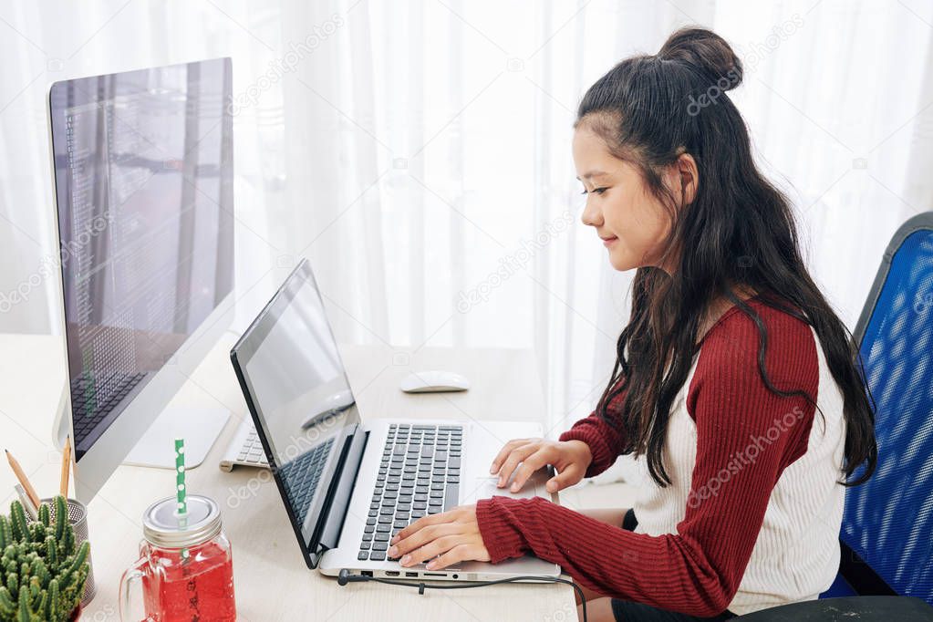 teenager girl sitting at desk in front of computer with laptop 