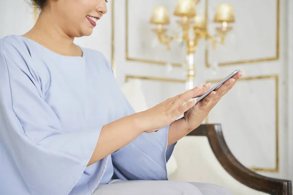 Close-up of young woman holding mobile phone in her hand and typing online message while sitting on sofa at luxury hall