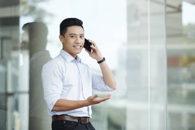 Genç gülümseyen Asyalı iş yöneticisi nin portresi telefonda konuşuyor ve kameraya bakıyor