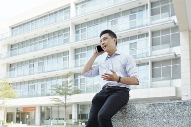 Ofis binasının önünde oturan ve cep telefonuyla bir şeyler açıklayan işadamı