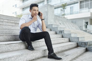 Pozitif Vietnamlı işadamı ofis binası yakınında adımlar üzerinde oturan ve telefonla arama