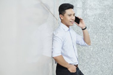 Beyaz gömlekli pozitif yakışıklı işadamı duvara yaslandı ve telefonla arıyor