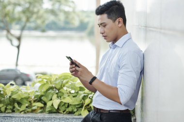 Ciddi genç Vietnamlı girişimci açık havada duran ve akıllı telefon bildirimleri kontrol