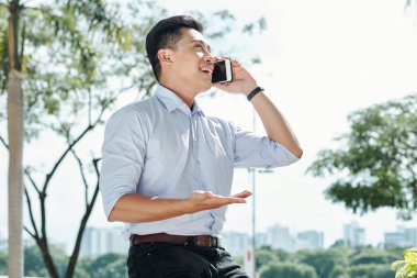 Mutlu heyecanlı Asyalı girişimci aktif telefonda açık havada konuşurken gesturing