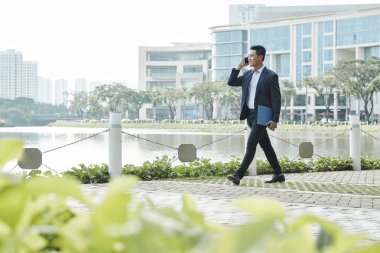 Şehirde nehir boyunca yürüyen ve cep telefonuyla konuşan yakışıklı gülümseyen işadamı 