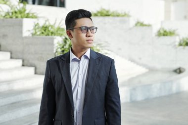 Büyük şehrin sokağında duran ve uzağa bakan gözlüklü genç dalgın girişimciportresi