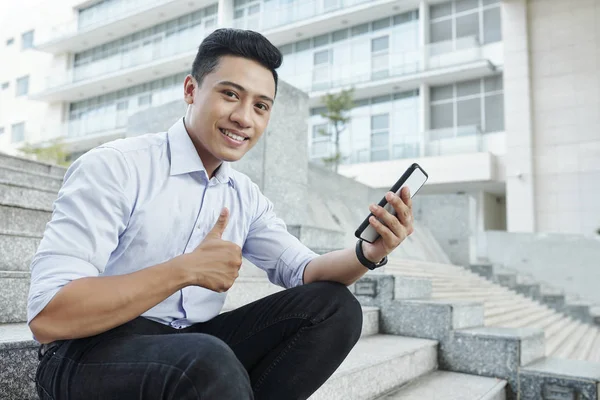 Portrét Mladého Usmívajícího Podnikatele Který Sedí Schodech Smartphone Rukama Ukazuje — Stock fotografie