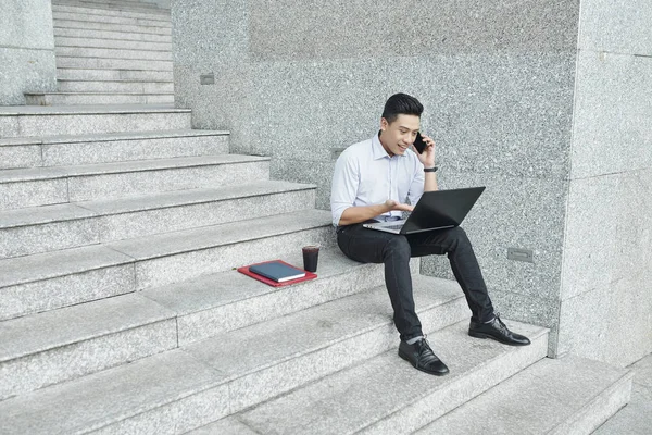 若い興奮ベトナムのビジネスマンは オフィスビルの階段に座って 電話でウェブサイトのインターフェイスを議論 — ストック写真