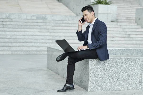 Usměvavý Vietnamský Podnikatel Který Sedí Venku Laptopem Volá Spolupracovníka Nebo — Stock fotografie