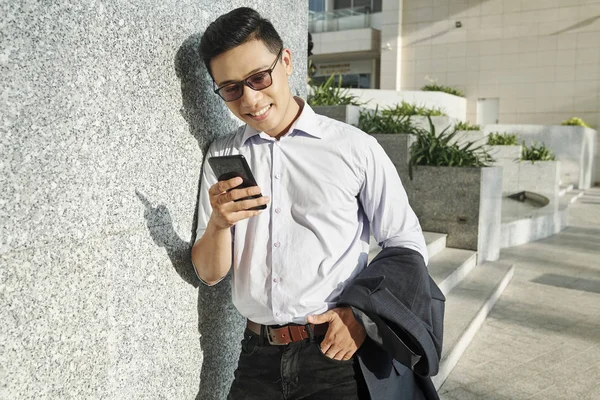 幸せな若いベトナムの起業家は 壁に傾いて 彼のスマートフォンでソーシャルメディアをチェック — ストック写真