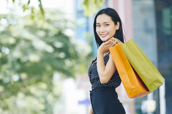 肖像亚洲美丽的女孩与购物袋微笑在相机 而站在城市 — 图库照片