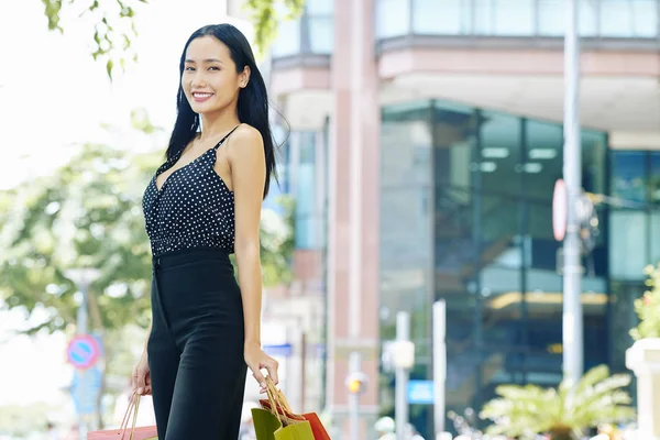 夏の街を歩きながらカメラに笑顔の買い物袋を持ったスタイリッシュなスーツを着たアジアの若い女性の肖像 — ストック写真