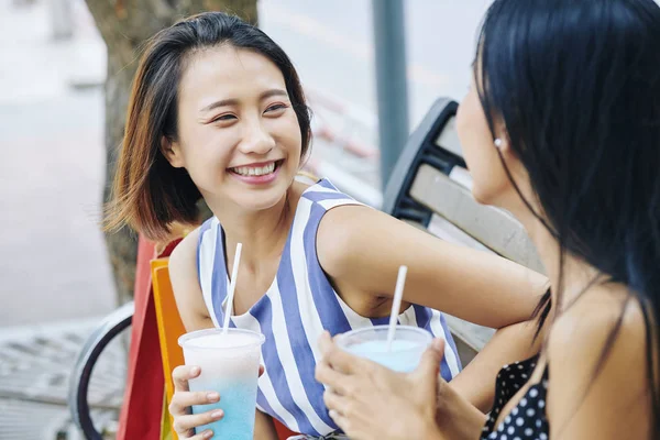 快乐的亚洲女人喝着新鲜的鸡尾酒 微笑着给她的朋友 而他们坐在公园的长椅上 — 图库照片