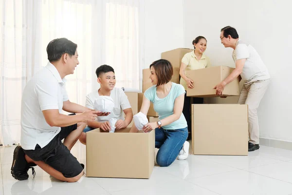 Cheerful big Vietnamese family packing belongings in cardboard boxes to move out
