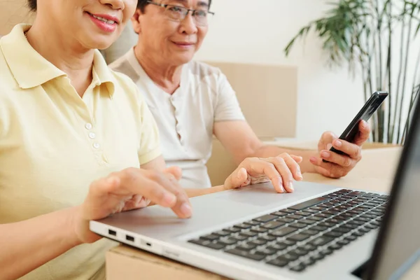 Akıllı Telefonlu Gülümseyen Asyalı Yaşlı Çift Evde Dizüstü Bilgisayarda Çalışıyor — Stok fotoğraf