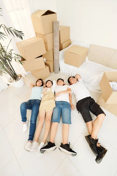 Dreamy smiling Vietnamese family of four resting on the floor and packing all belongings