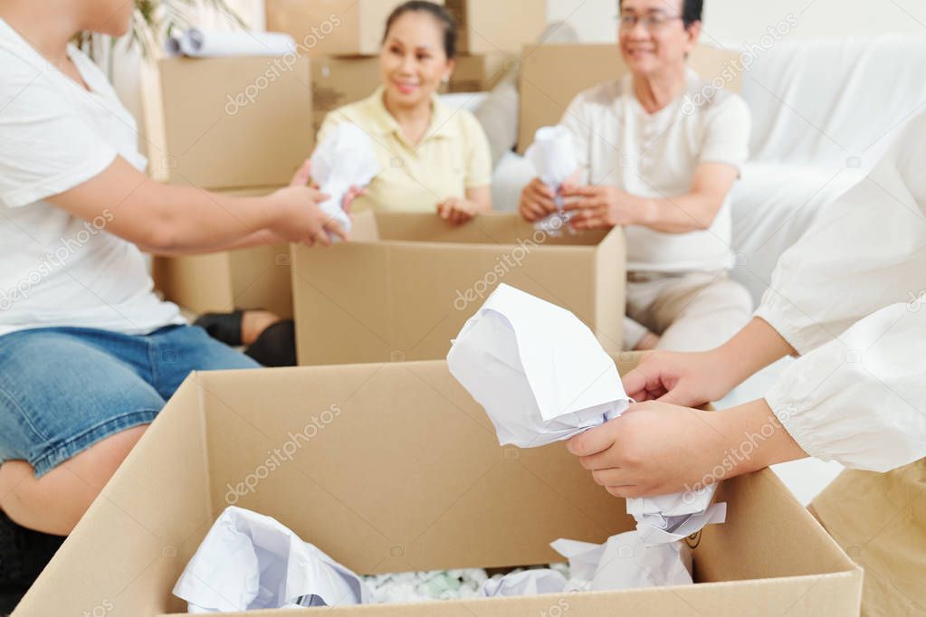 Family wrapping fragile tableware in paper when packing things in cardboard boxes