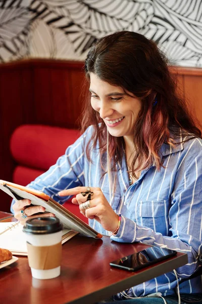 Laughing young woman sitting at cafe table and looking digital tablet computer