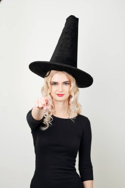 Cadı şapkalı, siyah bluzlu güzel sarışın kadın işaret parmağıyla kameraya bakıyor.