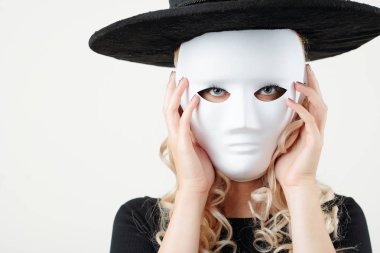 Cadı şapkalı, plastik maskeli ve kameraya bakan ciddi bir genç kadın.