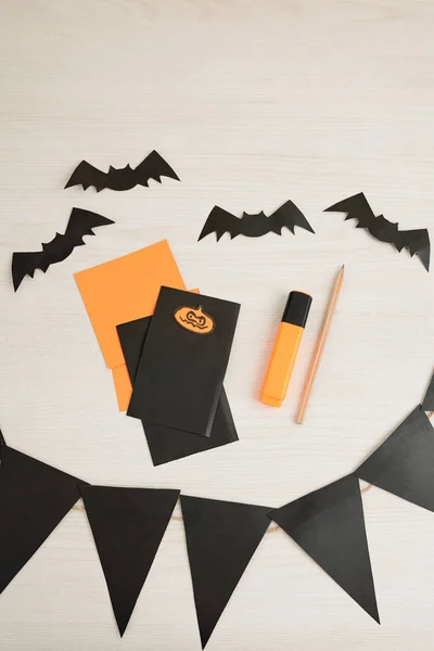 Halloween garland, paper bats and party invitations on table, view from above