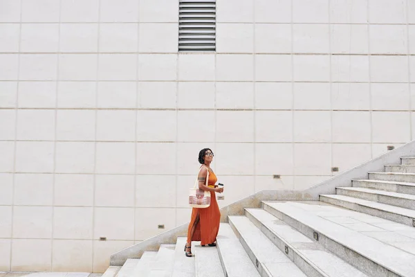 非洲快乐的女人穿着雅致的橙色衣服 手里拿着咖啡 走上楼去 — 图库照片