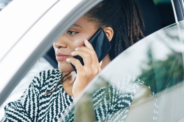 Afrikalı ciddi bir kadın arabasını sürerken yolda durup telefonla konuşuyor.