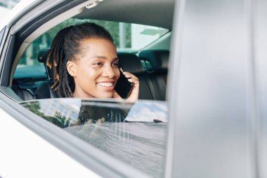 Arka koltukta oturan ve arabada cep telefonuyla konuşan mutlu Afrikalı kadın.