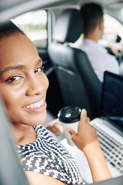 車の中でノートパソコンとコーヒーと後部座席に座っている間 アフリカの女性の笑顔の肖像画 — ストック写真