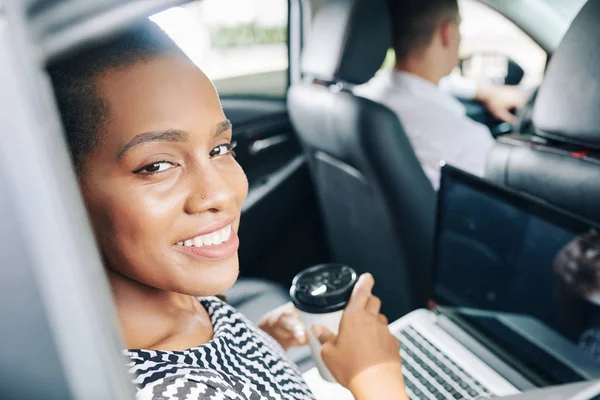 車で旅行中にノートパソコンとコーヒーを飲みながらカメラで微笑む若いアフリカ人実業家の肖像画 — ストック写真