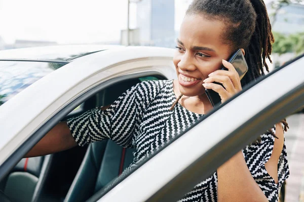 Şehirdeki arabasında oturan Afrikalı genç iş kadını cep telefonuyla konuşuyor.