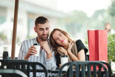 Kafe masasında erkek arkadaşıyla oturan ve ona hediye olarak verdiği sıcak süveteri tutan mutlu genç bir kadın.